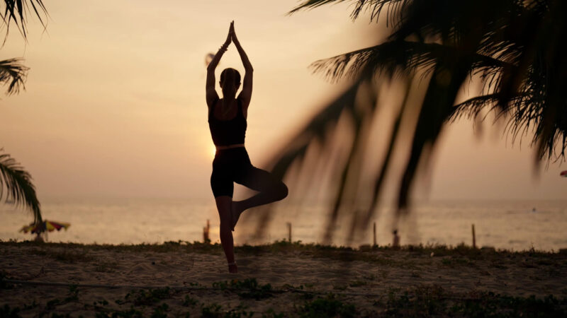 Practicing the tree pose on a beach at sunset